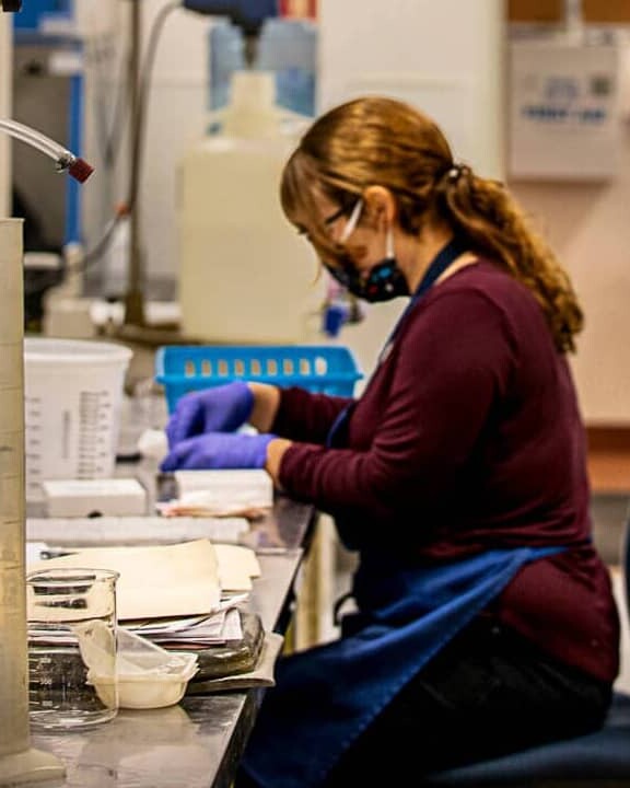 woman with face mask and protective gloves working at a table with scientific equipment