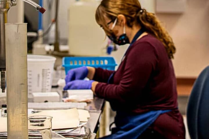 woman with face mask and protective gloves working at a table with scientific equipment