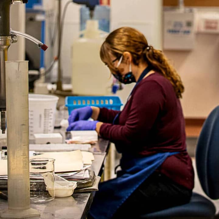 woman with face mask and protective gloves working at a table with scientific equipment