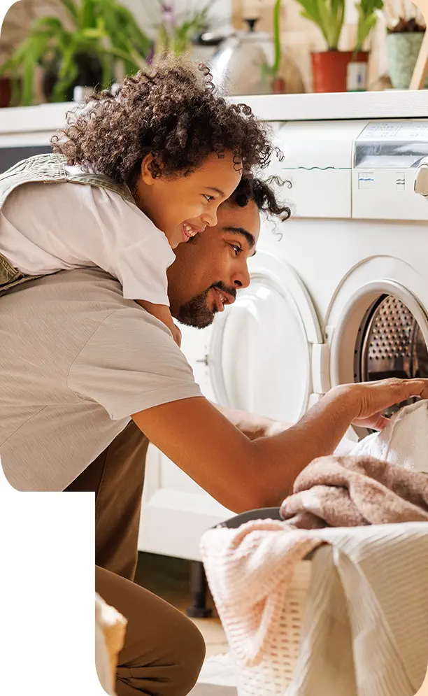 man removing laundry from dryer with child on back