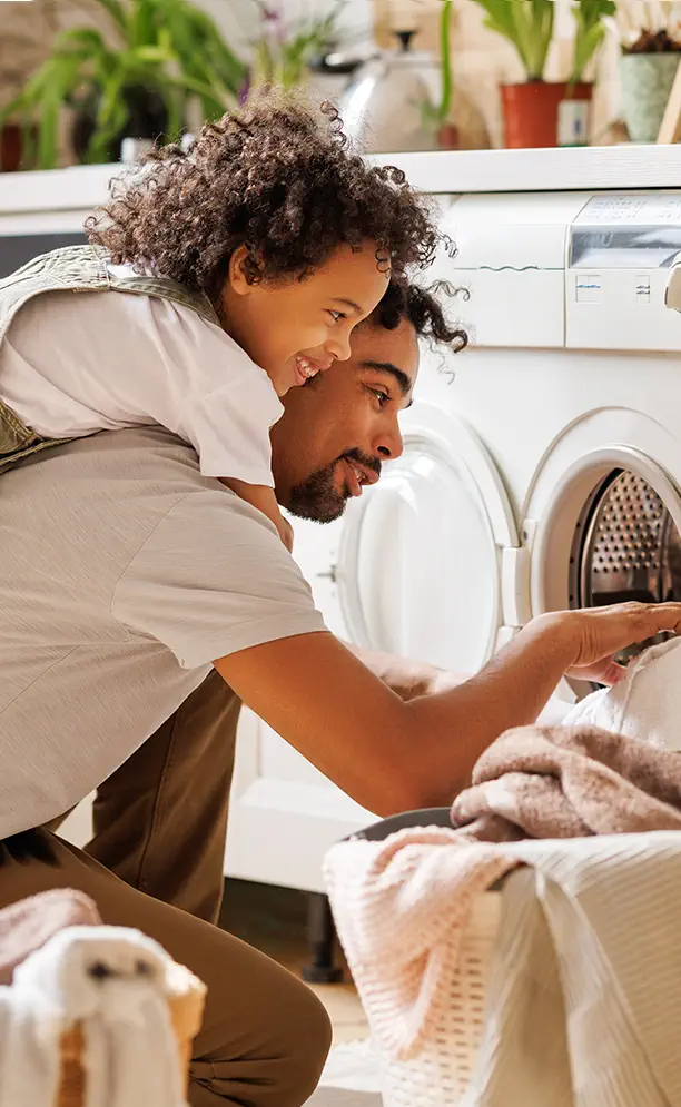 man removing laundry from dryer with child on back